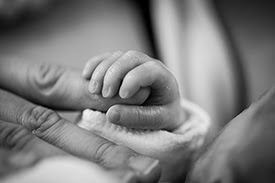 A newborn child holding onto it's mother's fingers
